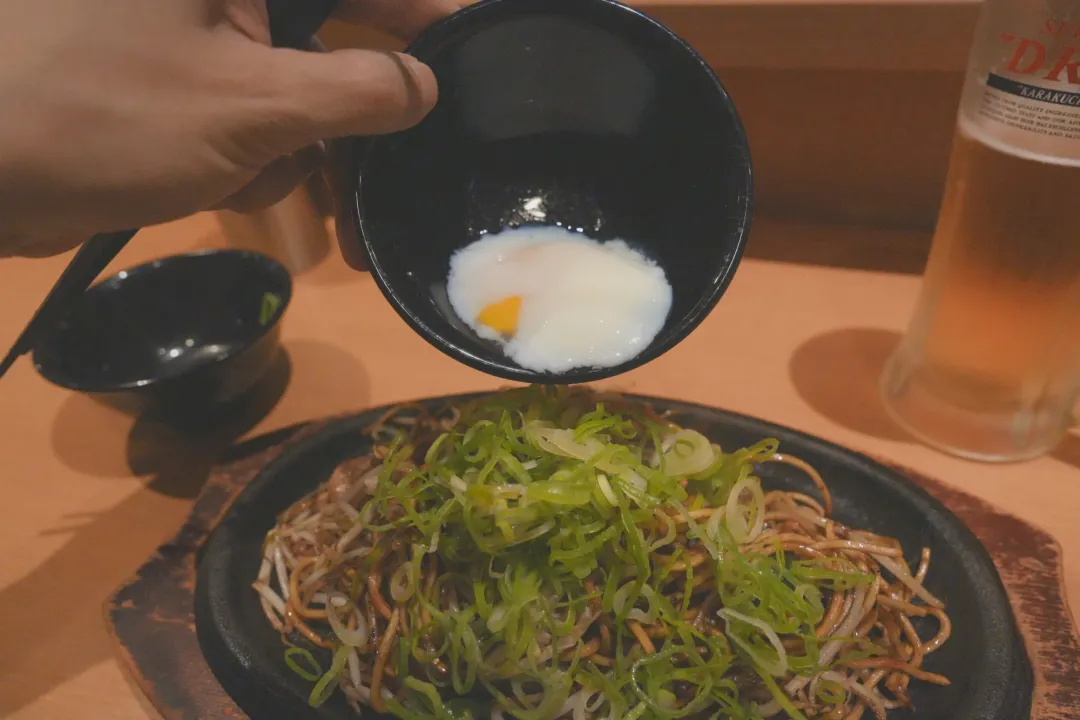 파를 올린 야키소바 위에 달걀을 붓는 모습