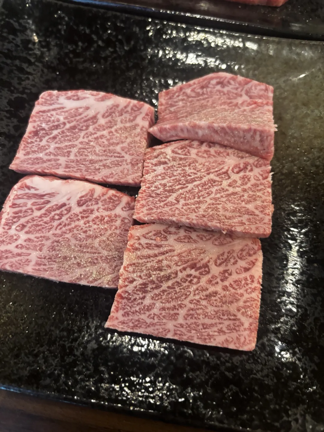 두툼하게 썬 마블링 소고기 다섯 점이 담긴 검은 접시